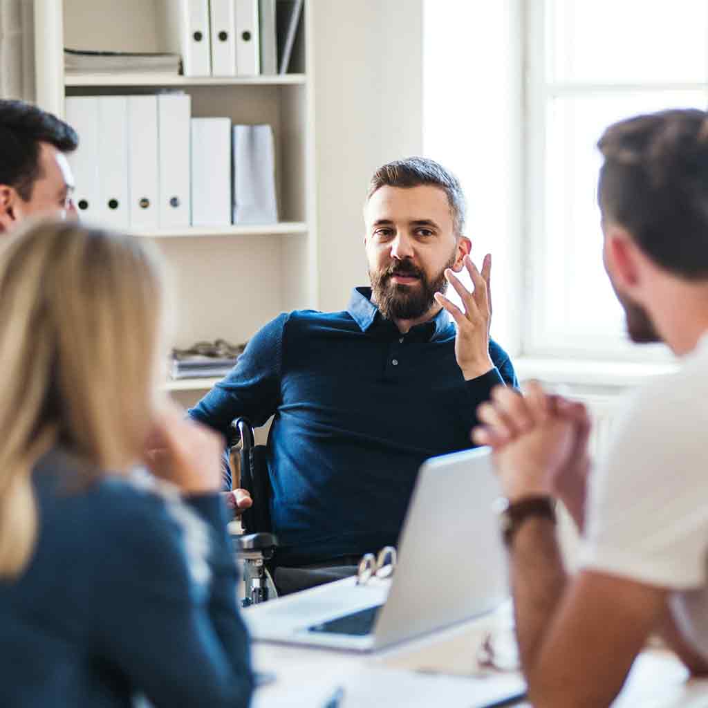 Group of staff sitting around a desk, One man is talking with expressive hand gusture