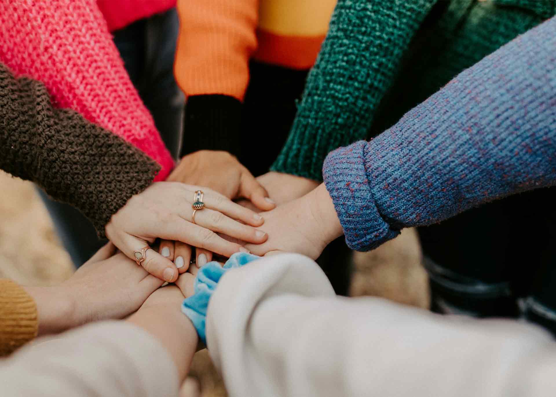 Arms in coloured jumpers outstretched with their hands on top of each other