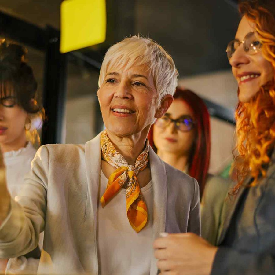 Manager and staff in funky business attire talking in front of a glass window post it notes on it.